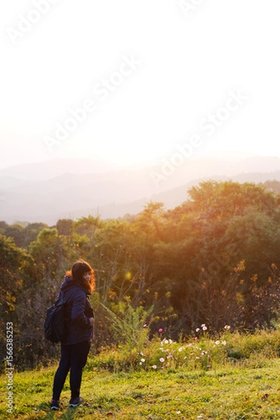 Fototapeta Asian young woman backpack smiling and standing with wildflower and beautiful landscape of valley Doi Luang Chiang Dao mountain, Chiang Mai Province of Thailand

