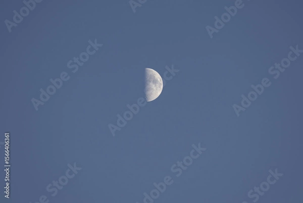 Fototapeta Riga, Latvia 05-09-2024 A Lone Moon Gazes Upward in the Endless Blue Sky