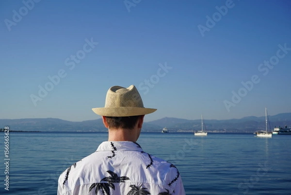 Obraz Relaxing by the serene waterfront, a person enjoys the calmness of the early morning, gazing at distant boats and the bright blue sky in a tropical paradise