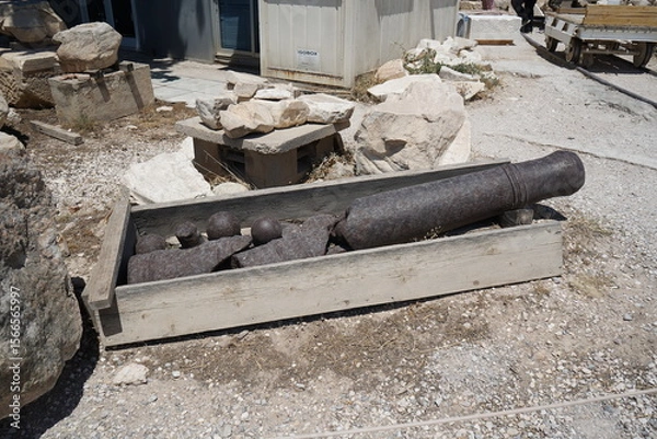 Obraz Ancient artillery remnants lie casually in a wooden crate at a historical excavation site near the coast on a bright sunny day