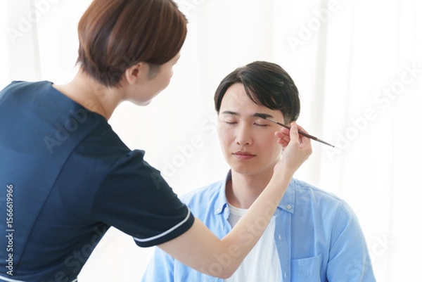 Fototapeta 美容部員に眉毛のメイクをしてもらう男性