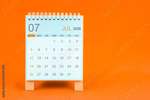 Fototapeta July 2026 desk calendar stand on orange color textile background.