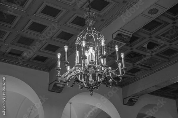 Obraz Vintage European Style Brass Chandelier with an Ornate Ceiling Background in Black and White.