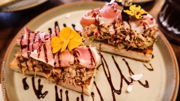 Fototapeta close up of a toast with tuna and ham, decorated with edible flower on top and with vinegar suace 