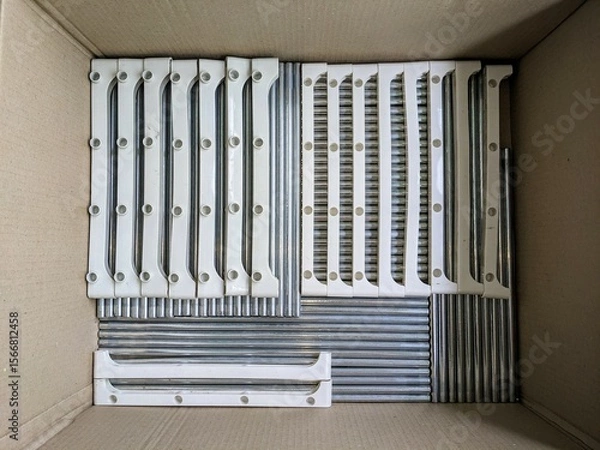 Fototapeta Metal rods and plastic components of a disassembled shelf, tidily arranged in a box. Organization and storage concept.