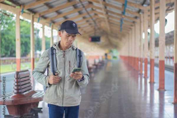 Fototapeta Confident young latin man standing alone at sunrise. Standing on train station platform, holding map. Confused but inspired. Travel, Direction, Exploring, Journey, Freedom, Lifestyle, Waiting, Serious