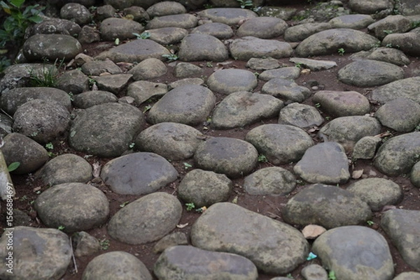 Fototapeta Close Up Stone Pathway. Traditional stone pathway in a rural Indonesian village. The path is made of large, rounded river stones meticulously arranged and bordered by stone retaining walls.
