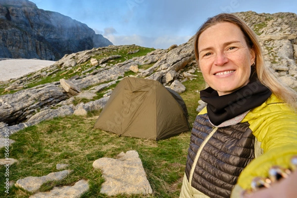 Obraz Selfie of a woman mountaineer next to a tent at sunset,