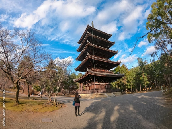 Obraz A female tourist taking a photo of the majestic five-storied pagoda at Ninna-ji Temple, captured in a dynamic wide-angle shot that emphasizes the scale of the ancient architecture in Kyoto, Japan.