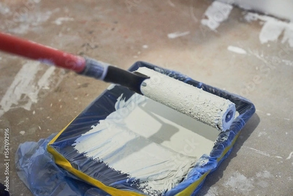 Fototapeta Apartment renovation. Concrete walls are painted gray with a paint roller. A container of paint for a paint roller. High quality photo
