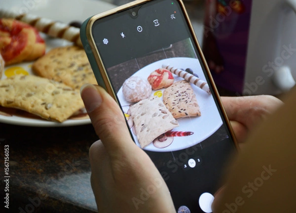 Obraz female hands holding smartphone and taking photo of sweet food. photo or video blogger. sweet and tasty dessert for kids and adults. cookies and candies on plate