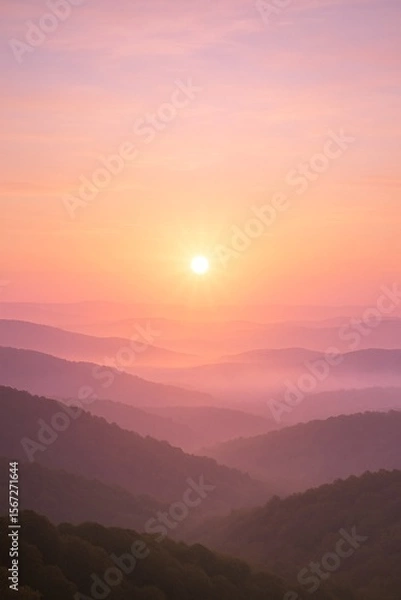 Fototapeta A tranquil sunrise paints soft pastel hues across rolling mist-covered mountains, creating a serene and dreamlike atmosphere.

