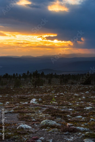 Fototapeta A breathtaking fiery sunset casts golden hues across the rugged mountains of Sweden and Norway. Heavy clouds loom above as the landscape darkens, revealing rocky terrain below