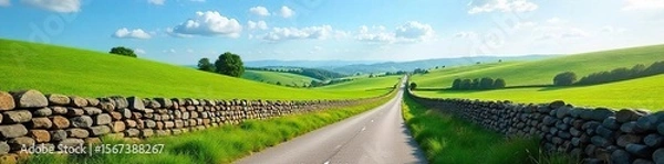 Fototapeta Tranquil Country Lane Winding Through Rolling Green Hills and Ancient Stone Walls Under a Vibrant Blue Sky