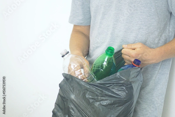 Fototapeta Man holding garbage bag filled with used empty plastic bottles. Recycling habits and global pollution crisis. Responsible behavior of a modern person: collection and separation of household waste.