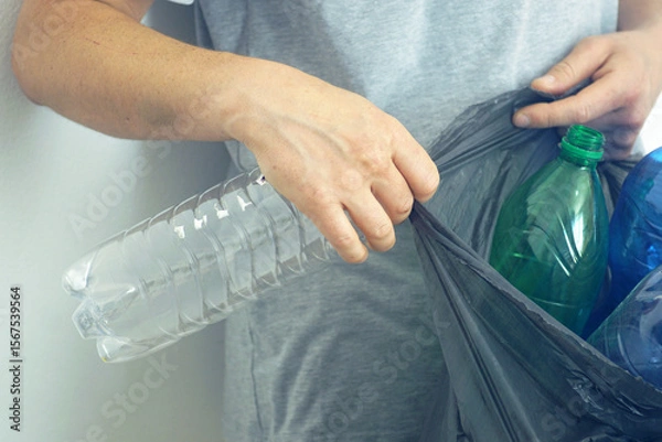 Fototapeta Waste separation: a man collects empty bottles in a garbage bag for subsequent recycling, close-up of hands. Concept of everyday eco-friendly actions, individual impact on environment and zero-waste
