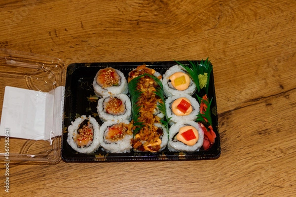 Obraz Set of sushi rolls in plastic box on wooden table. Sushi for take away or delivery of sushi in plastic container