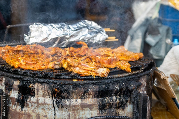 Fototapeta Sizzling chicken grilling over hot coals at streetside barbecue in Tortuguero, Costa Rica's vibrant coastal village