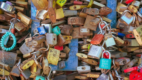Fototapeta Cluster of colorful padlocks symbolizing love and commitment, attached to metal fencing.
