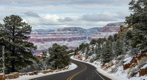 Fototapeta A winding road descends into a snow-dusted canyon, revealing layered rock formations under a cloudy sky (1)