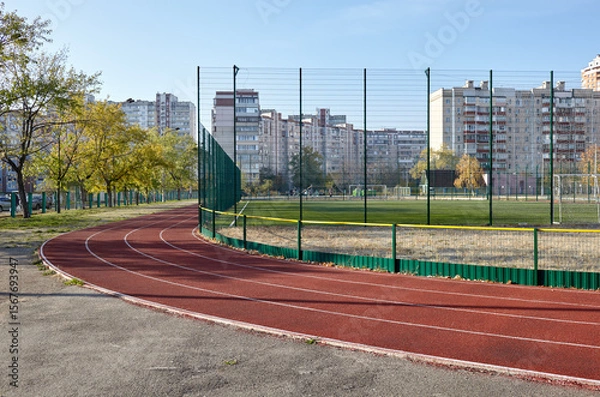 Fototapeta Red treadmill on sport field. Landscape of soccer field with green grass and running track