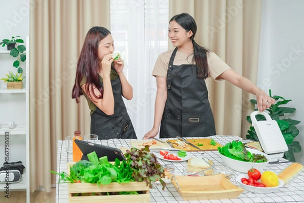 Fototapeta Two asian woman study online in the classroom making sandwich together in the home kitchen. Homemade and Learn online concept	