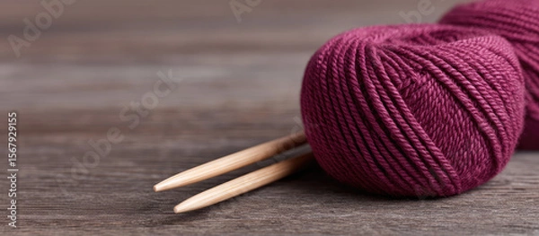 Obraz A ball of burgundy yarn with wooden knitting needles rests on a wooden surface. Crafting, knitting, hobby, yarn