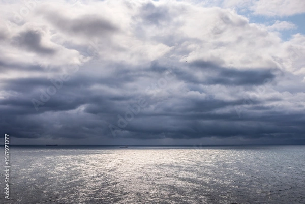 Fototapeta Stormy clouds gather over the North Sea near Denmark, as seen from a cruise ship. The silver water reflects light through breaks in the dark sky.