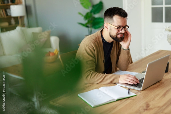 Fototapeta Young Caucasian Man Working from Home on Laptop in Bright Living Room with Relaxed Atmosphere
