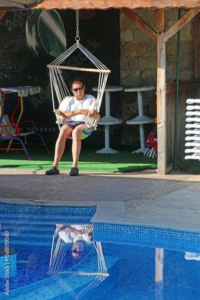 Fototapeta Man in a swing chair by a swimming pool