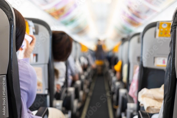 Obraz Inside commercial airplane, passengers sit calmly in economy class. Selective focus of the aisle, with blurred seats creating depth. It shows air travel, aviation lifestyle, or transportation scenes.