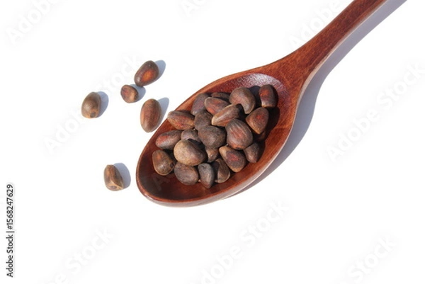Fototapeta On a white background lies a wooden spoon with pine nuts.