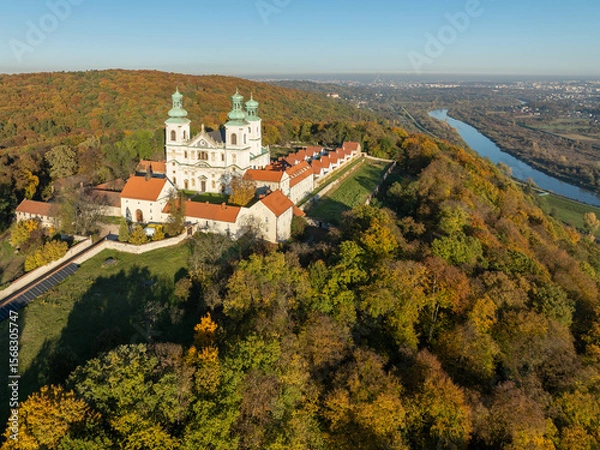 Fototapeta Active Camaldolese monastery and baroque church in a wood on the hill in Bielany, Krakow, Poland. Aerial view in sunset light in fall with Vistula River and far view of Cracow city in the background