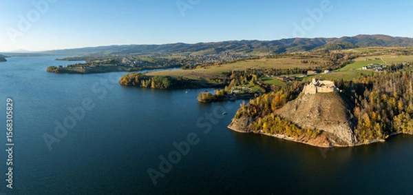 Fototapeta Poland. Wide aerial drone panorama of artificial Czorsztyn lake with gulfs and peninsulas, ruins of medieval Czorsztyn castle and Gorce mountain range in the background. Autumn colors, sunset light