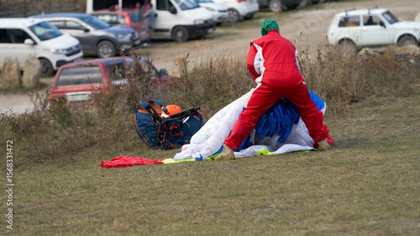 Fototapeta A paraglider assembles his paraglider after landing. In the background is a parking lot.