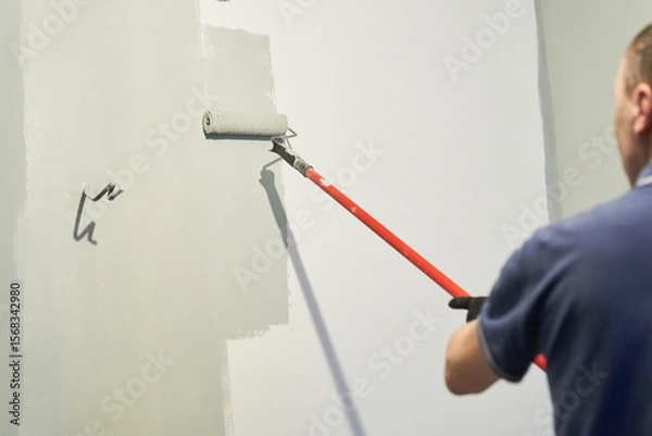 Fototapeta Men's hands paint walls with a roller, work painting on the surface, painting walls in an apartment, repair with white paint. With space to copy. High quality photo