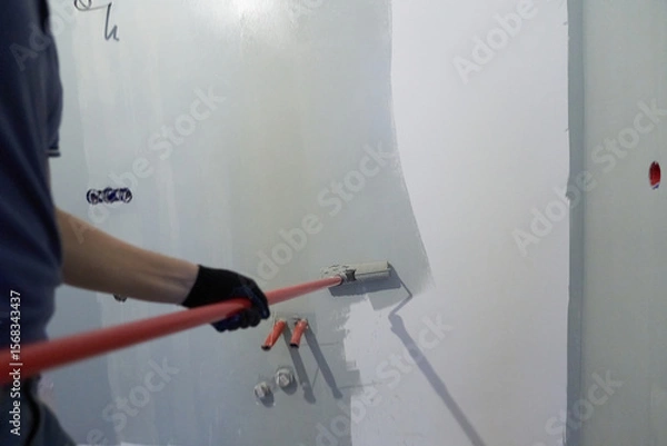 Fototapeta A man paints the inner wall of his house. Apartment renovation. Concrete walls are painted with a paint roller. High quality photo