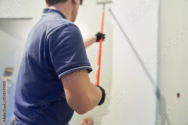 Fototapeta Men's hands paint walls with a roller, work painting on the surface, painting walls in an apartment, repair with white paint. With space to copy. High quality photo