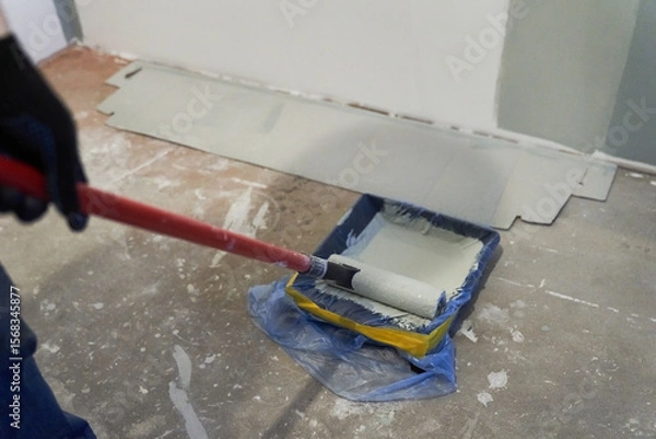 Fototapeta A container of paint for a paint roller. Apartment renovation. Concrete walls are painted gray with a paint roller. High quality photo