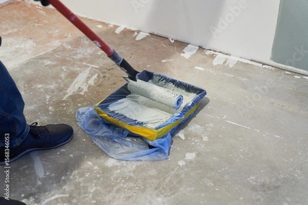 Fototapeta A container of paint for a paint roller. Apartment renovation. Concrete walls are painted gray with a paint roller. High quality photo