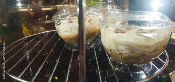 Obraz Sweet fruit and cream dessert on a glass spinning display case in a cafe. Cold dessert, ice cream.