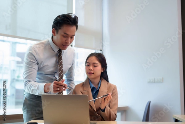 Fototapeta Asian business professionals discuss project analysis strategy on laptop during collaborative office meeting