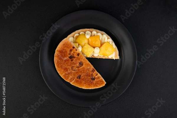 Fototapeta Cake with fruit on a black plate, isolated on black background