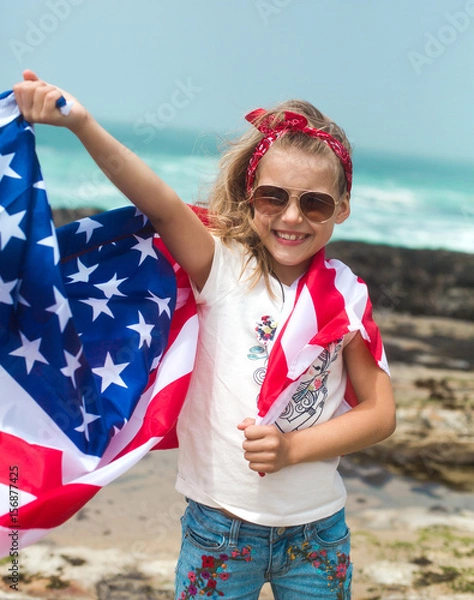 Obraz Little smiling girl with long blond hair holds flying American flag on US Independence Day.