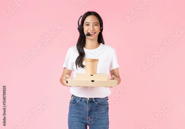 Fototapeta Studio shot of Beautiful Asian woman holding pizza boxes and consultant wearing microphone headset of customer support phone operator with isolated on pink background.