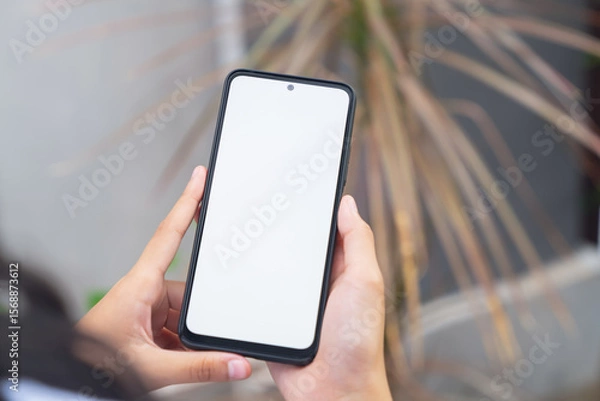 Fototapeta Hand holding smartphone with blank screen for graphic display montage on outdoors background, mockup display for lifestyle and wireless technology.