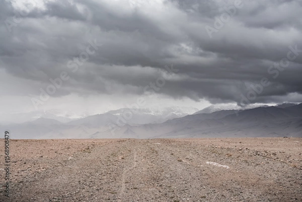 Fototapeta Panorama of mountain peaks with snow and glaciers, a landscape in the highlands of the Tien Shan in Pamir in cloudy weather with clouds and rain, high-mountain steppe and mountains in the background