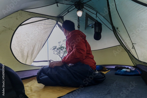 Fototapeta Men sat in a forest camping tent in the national park on the day of the rain and fog