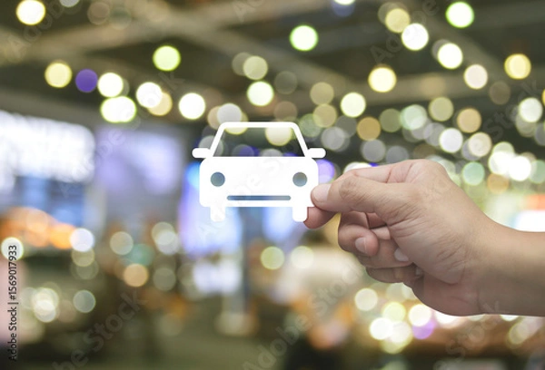 Fototapeta Hand holding car flat icon in fingers over blur light and shadow of shopping mall, Business transportation service concept