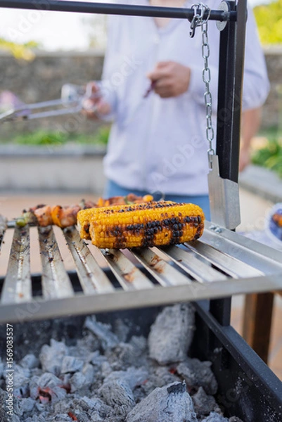 Fototapeta Grilling corn on the cob and chicken skewers on a barbecue grill